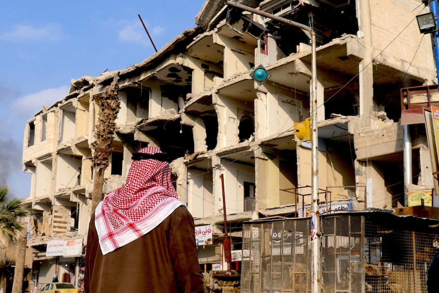 A man looks at the bombed-out wreck or an apartment