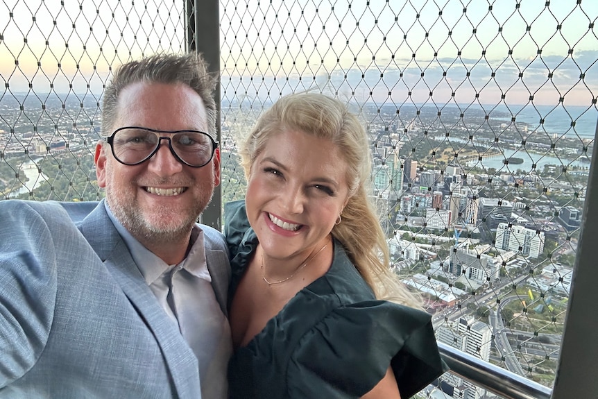 Lucy Durack with her husband Christopher Horsey as they smile for a selfie at the top of a tall building.