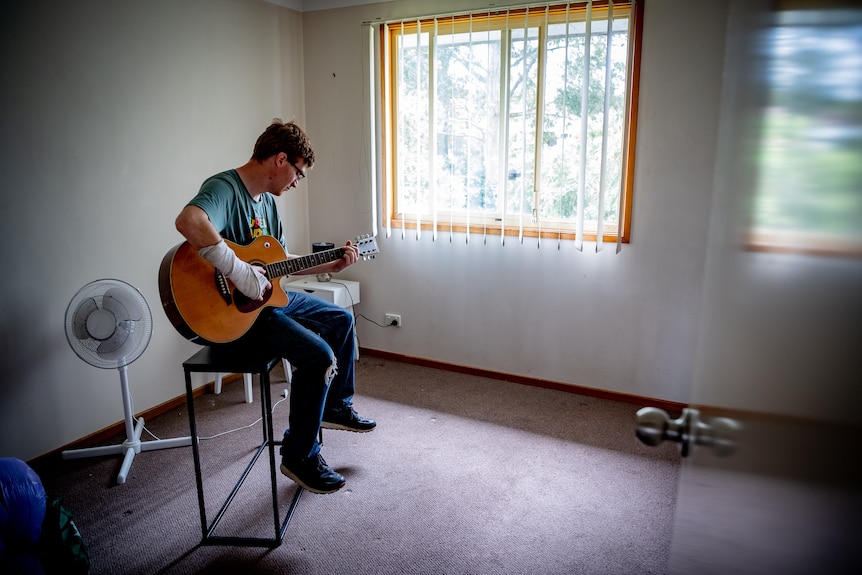 A young man sitting playing the guitar.