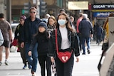 People on a street in Melbourne's CBD, including one wearing a face mask.