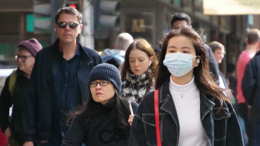 People on a street in Melbourne's CBD, including one wearing a face mask.