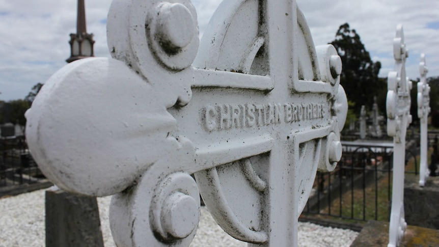 A close-up of a white Celtic cross with the words Christian Brothers written across the centre.