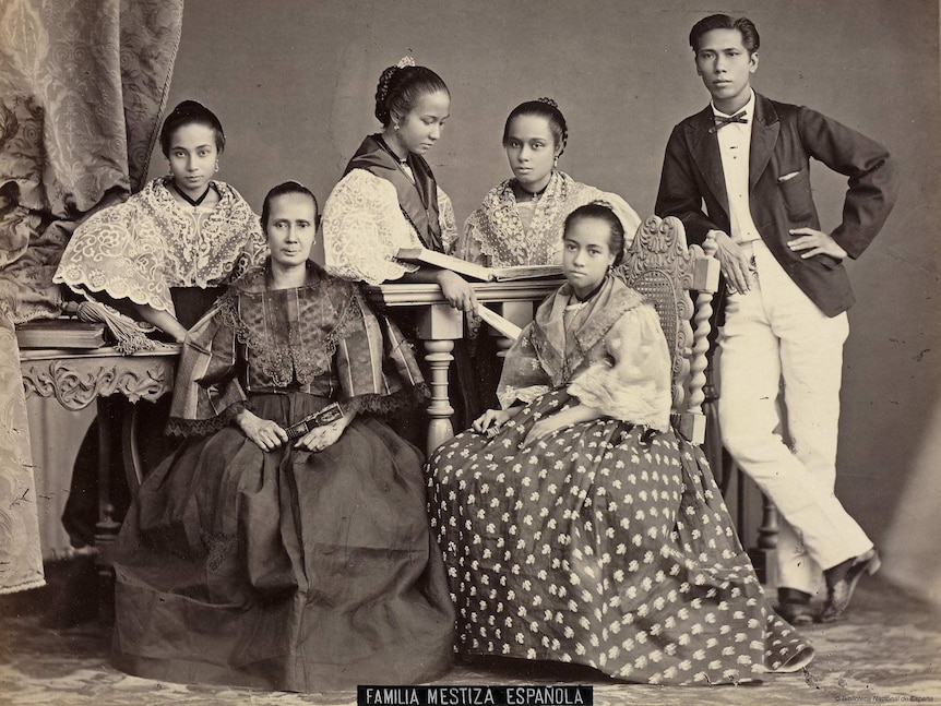 A black and white photo shows a Spanish-Filipino family pictured in ornate 19th-century clothing in a formal pose.