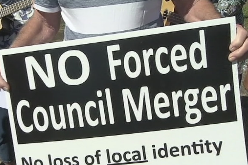 A sign reads 'no forced council merger'
