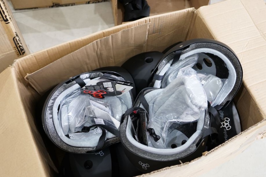A cardboard box filled with brand new black skating helmets.