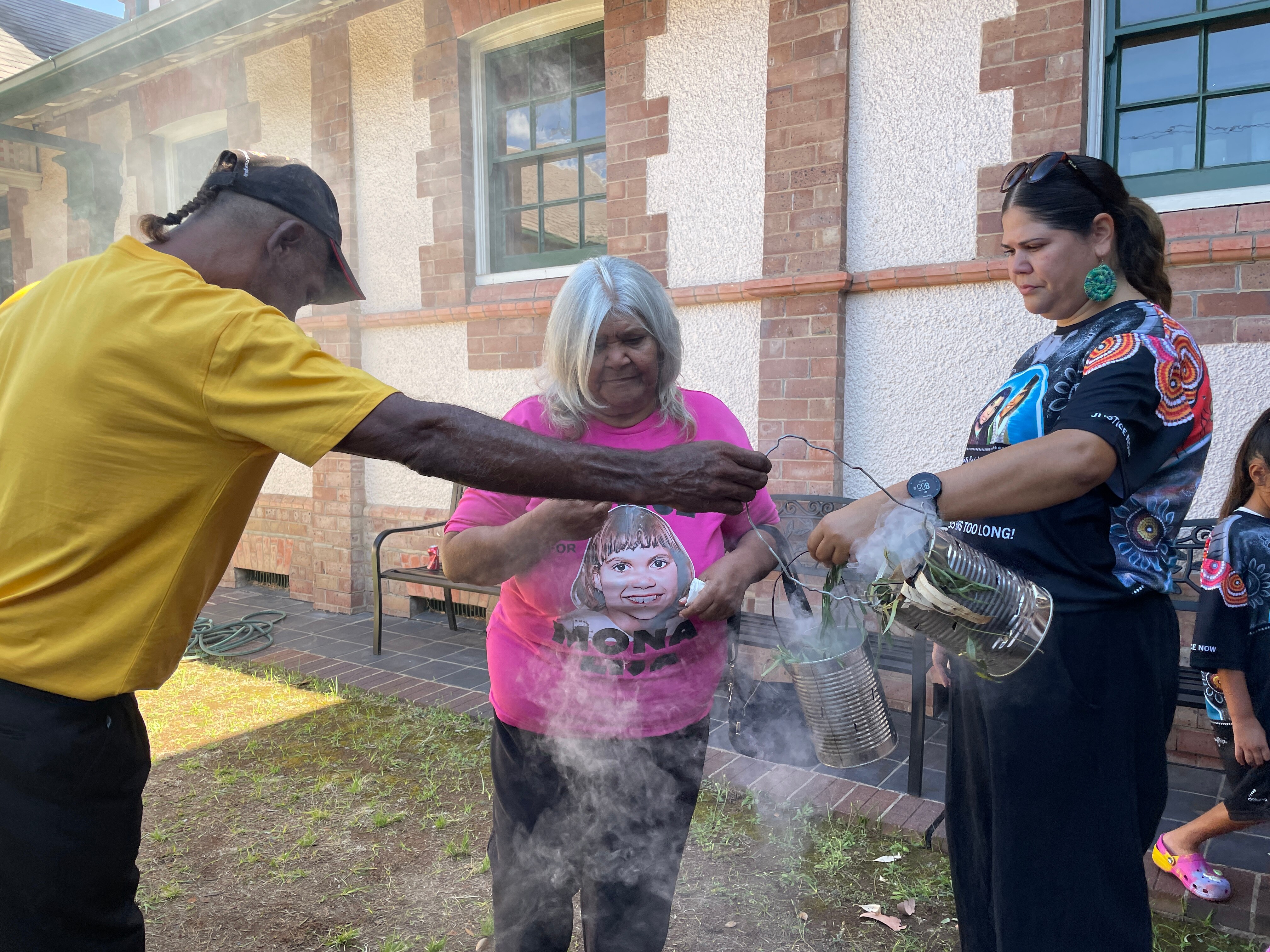An Indigenous woman surrounded by two people holding cans and smoke circling the air