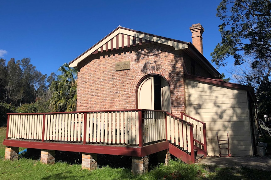 An old brick school building, with a wooden verandah around the front.