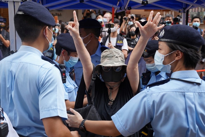 A woman in a mask holds up her hands in defiance while surrounded by police 