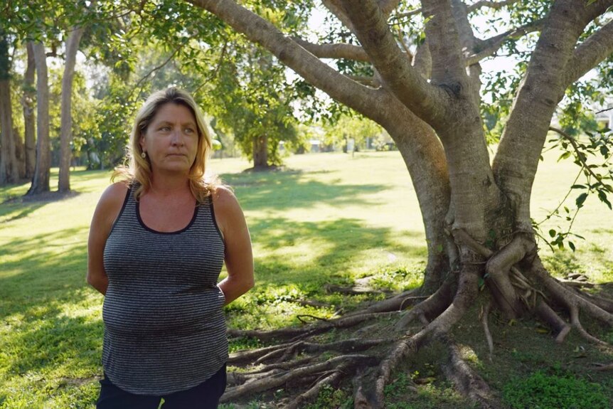A portrait of a woman with blonde hair standing outside under a large tree