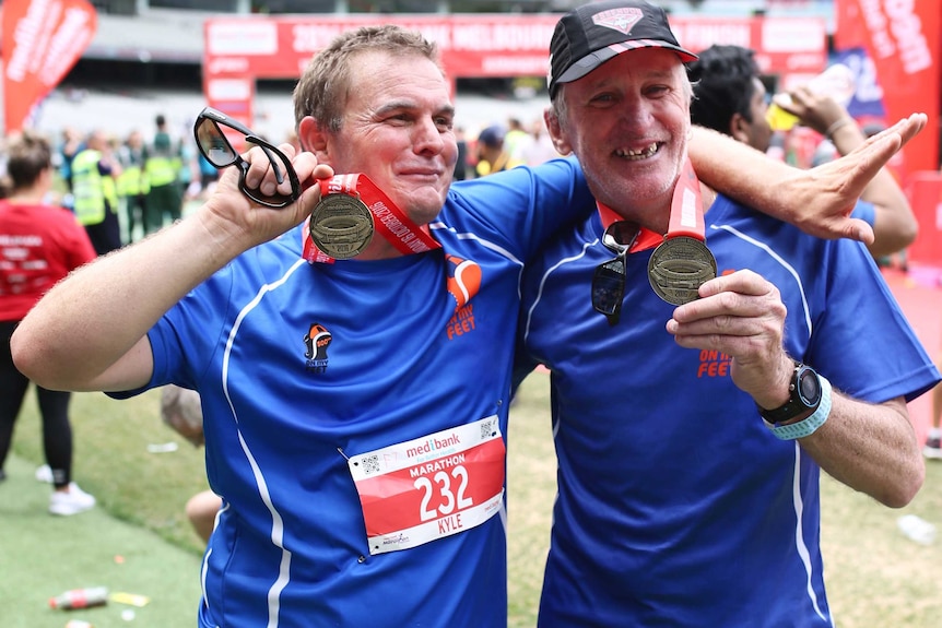 Ian Brown and Kyle Holtzman pose for a photo holding up their Melbourne Marathon medals at the end of the race.