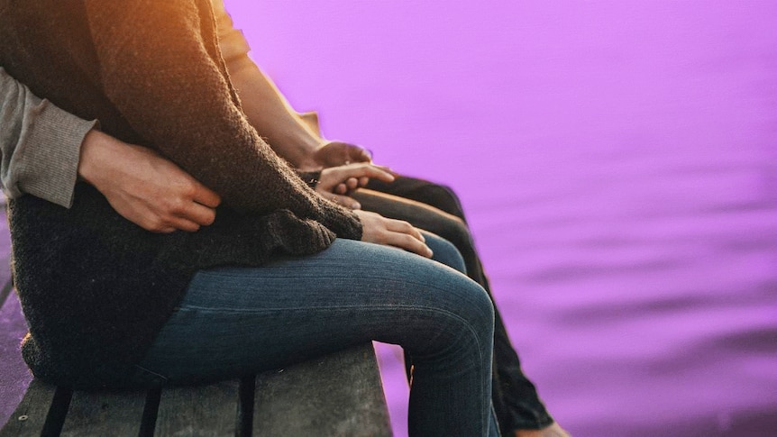 A man holding a woman around the waist as they sit on a pier to depict how to spot domestic violence and what to do.