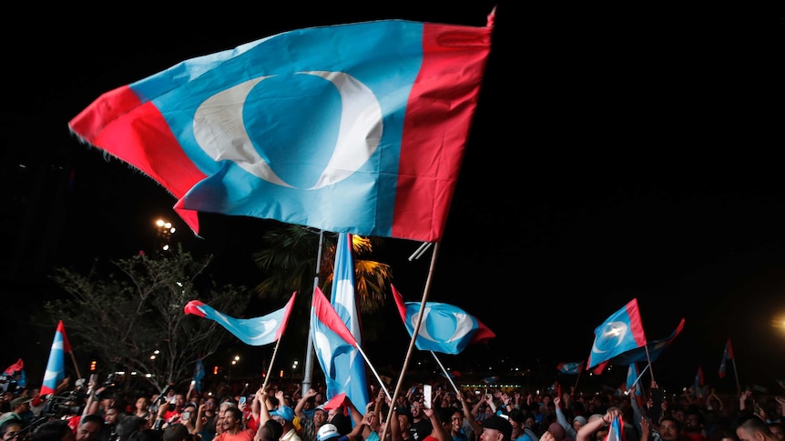 Opposition party supporters cheer and wave their party flags at a night time rally.