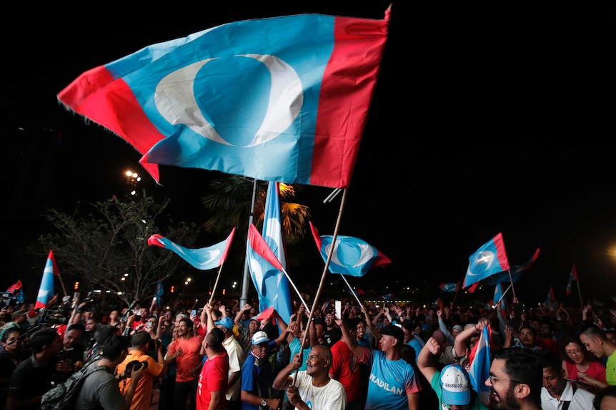 Opposition party supporters cheer and wave their party flags at a night time rally.