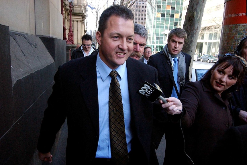 Paul Dale walking down the street in a suit, surrounded by journalists.