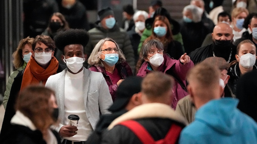 People walk down a crowded street wearing face masks