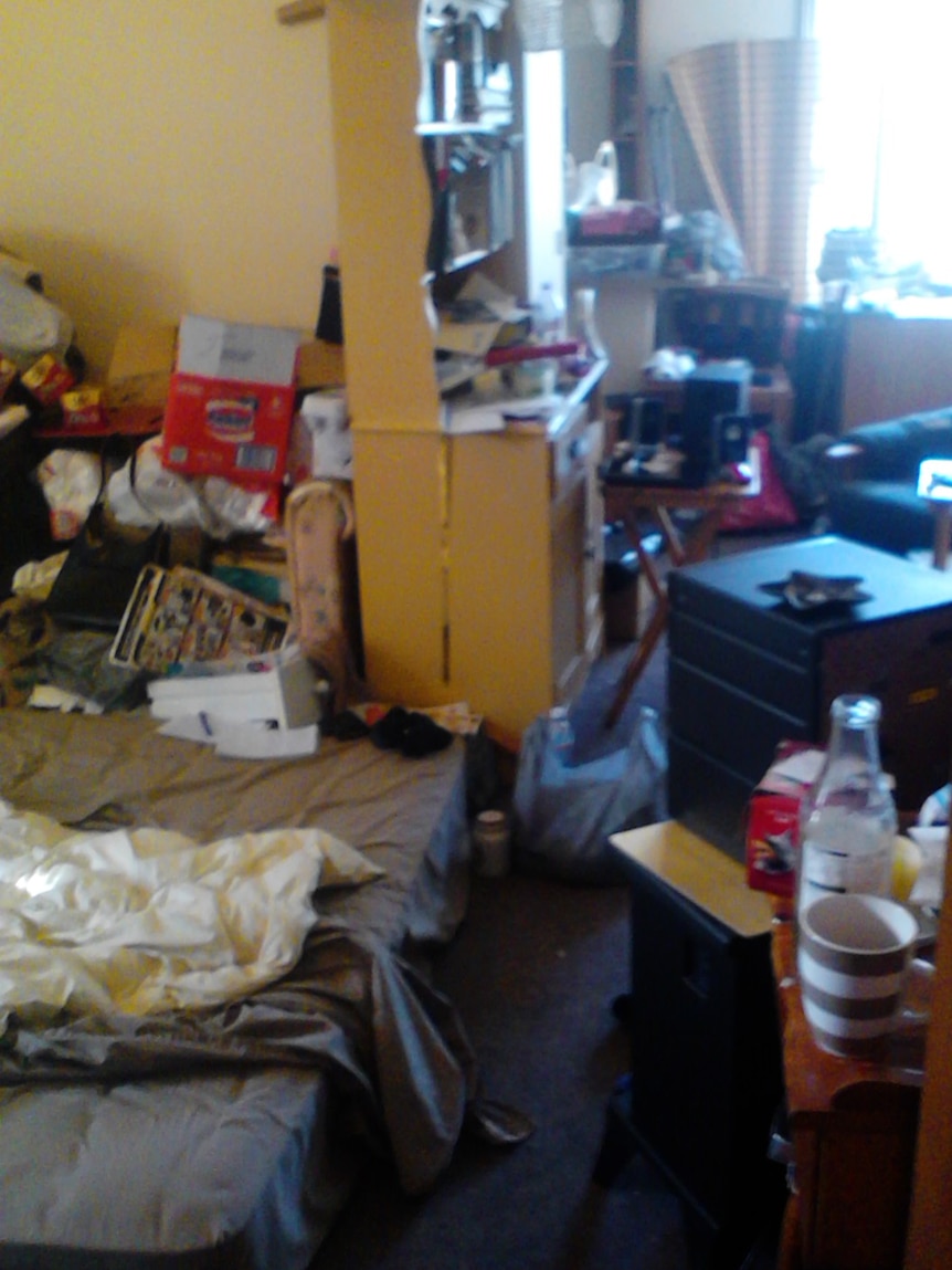 A hoarded living room, rubbish and empty cups are evident.