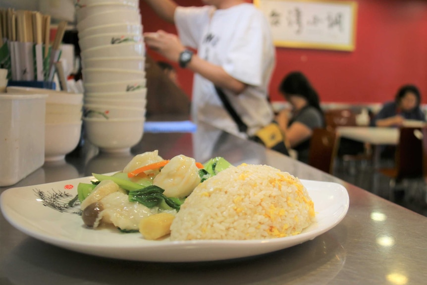 A plate of stir fry vegetables and rice on a bench of a restaurant