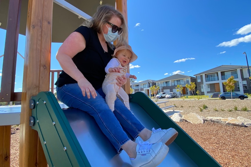 Jenny Quinn holds one-year-old Finn  on her lap as they prepare to go down a slide at a playground
