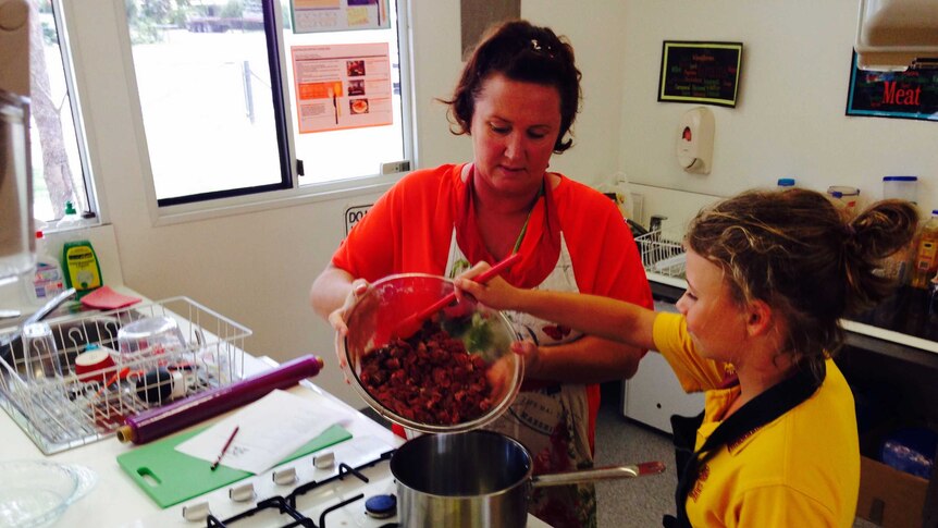 Biggenden teacher JT Foody and student Abbey Gibbs, 10, scoop meat into a saucepan in the school kitchen.