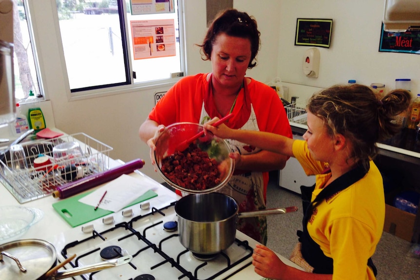 Biggenden teacher JT Foody and student Abbey Gibbs, 10, scoop meat into a saucepan in the school kitchen.