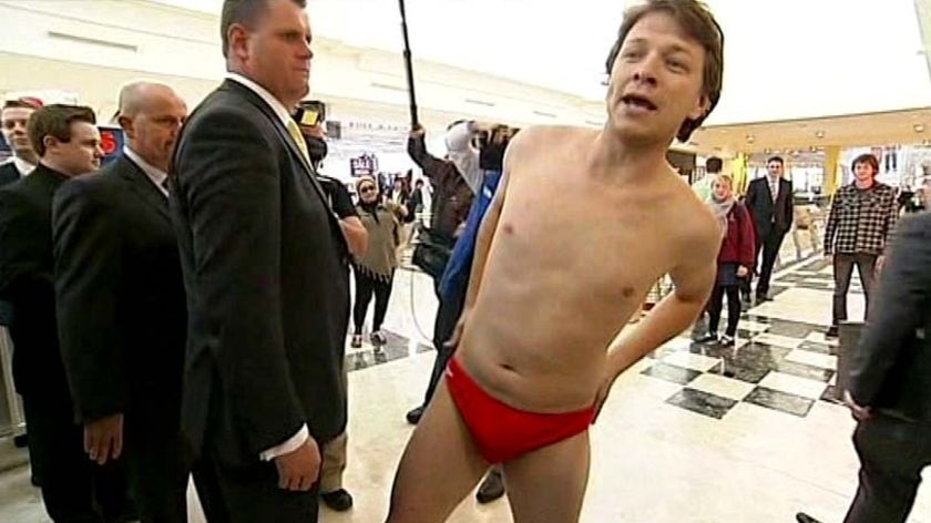 A Labor staffer wearing red speedos approaches Opposition Leader Tony Abbott