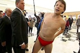 A Labor staffer wearing red speedos approaches Opposition Leader Tony Abbott