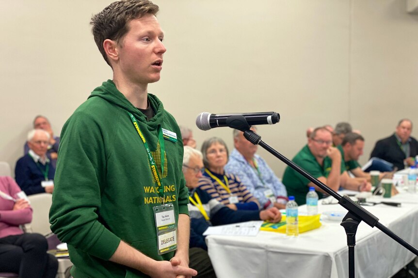 A young man in a green jumper speaks into a microphone.