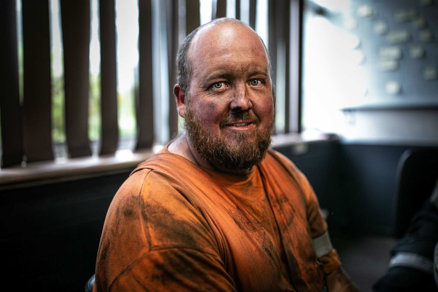 A bald man wearing a high-vis top and with soot on his face.