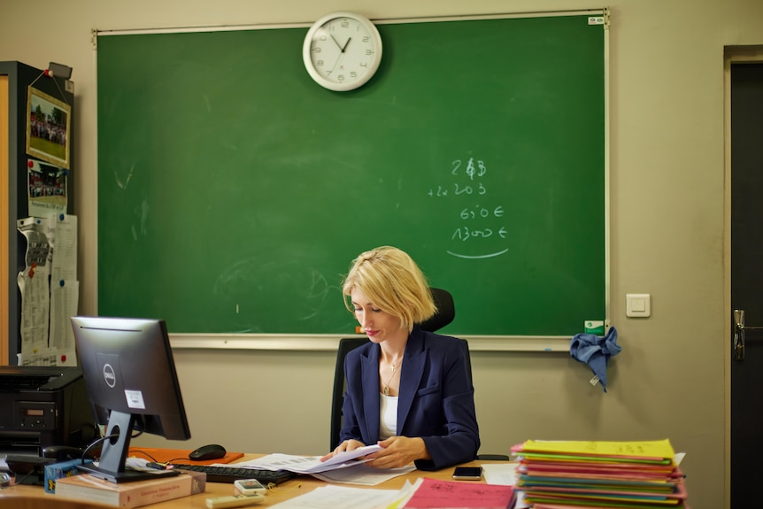 Géraldine sits at her desk in front of a blackboard immersed in her work.