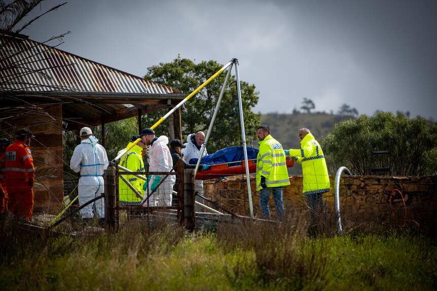 A group of people wearing white jumpsuits and high vis jackets removing a tarp covered object from a well 