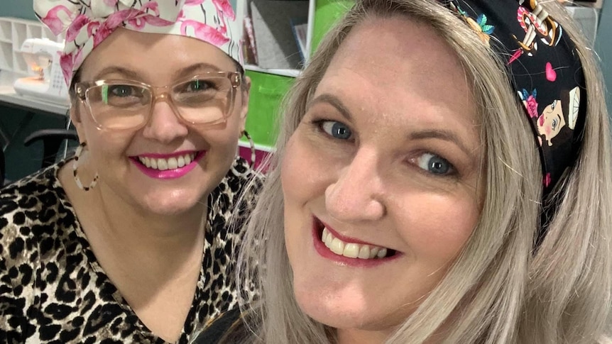 Two women with head bands look into the camera, smiling