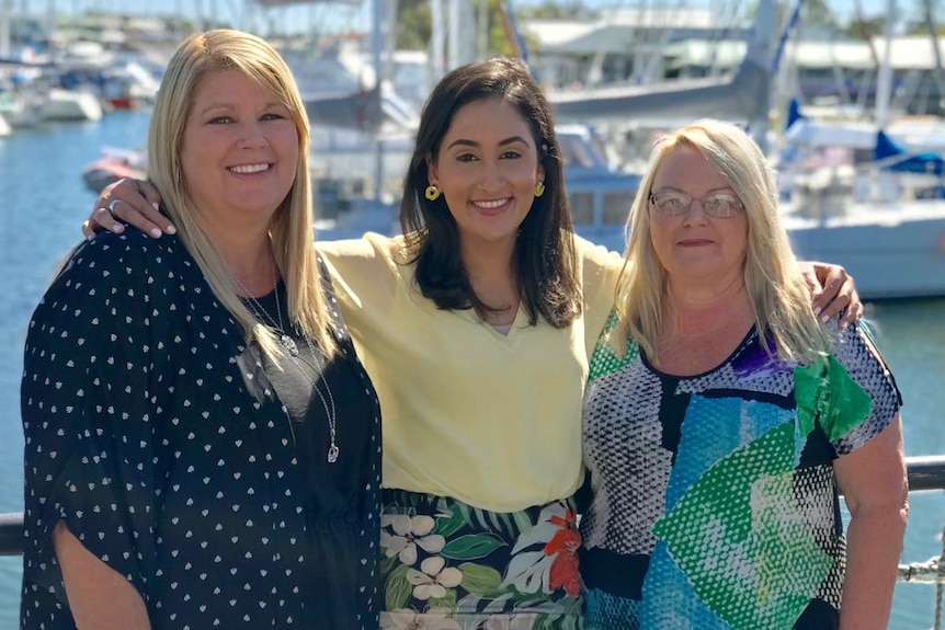 Del stands with two blonde-haired women at a marina