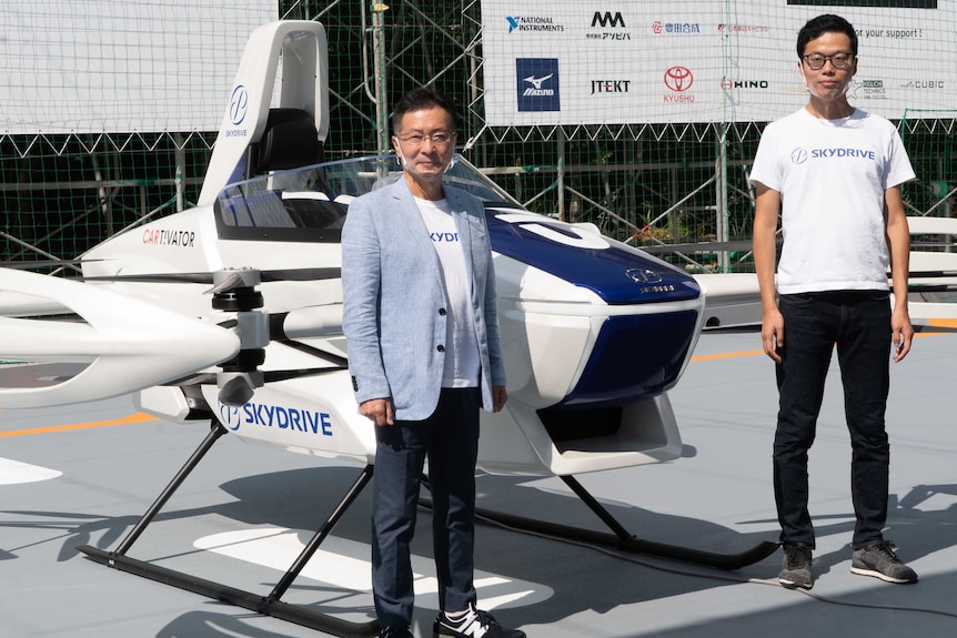 Two men standing next to a flying car prototype