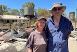 A couple with a fire-damaged structure behind them.