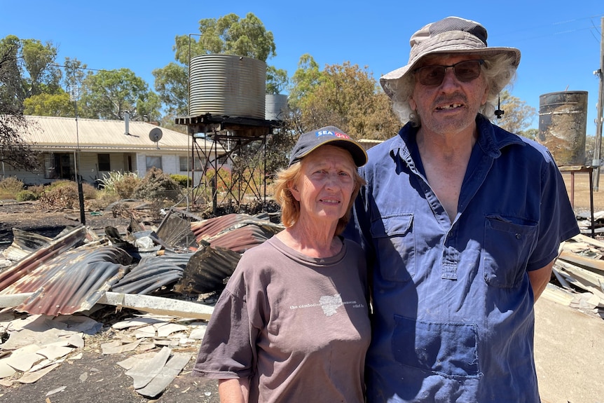 A couple with a fire-damaged structure behind them.