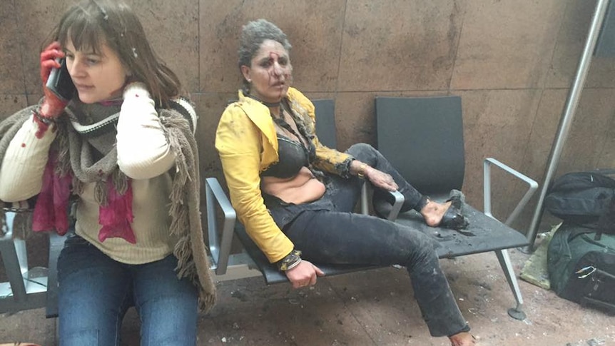 Two women sit on chairs bloodied, one woman is on the phone