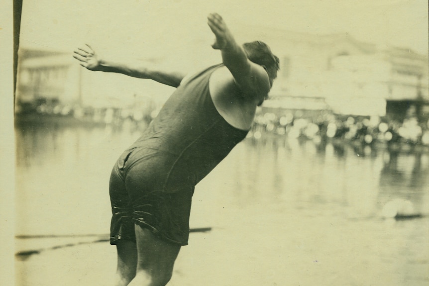 Fotografía en blanco y negro de un hombre en traje de baño que se zambulle en el agua desde un poste.