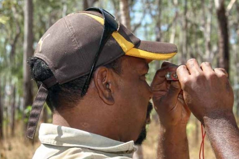 Willie Rioli Senior looks through a device to measure the height of a tree.