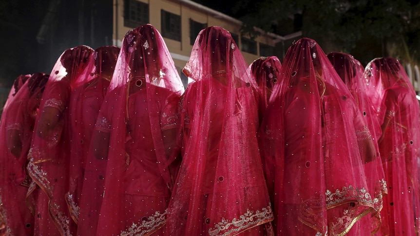 A group of women in traditional Indian dress with veils covering their heads face inwards in a crowd.