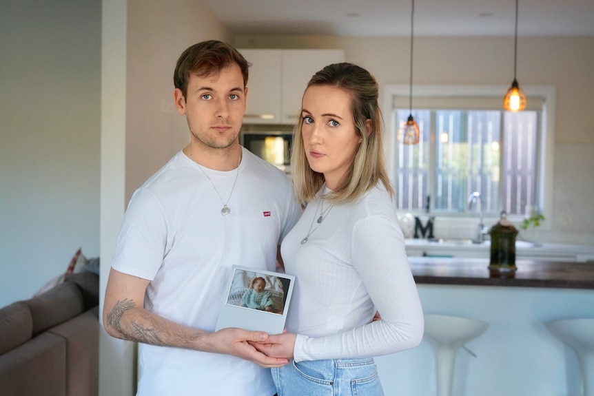 Dimity and Michael hold hands, standing in their living room.