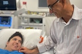 Fadel smiles down at his daughter Zahra who is in a hospital bed and smiling back up at him