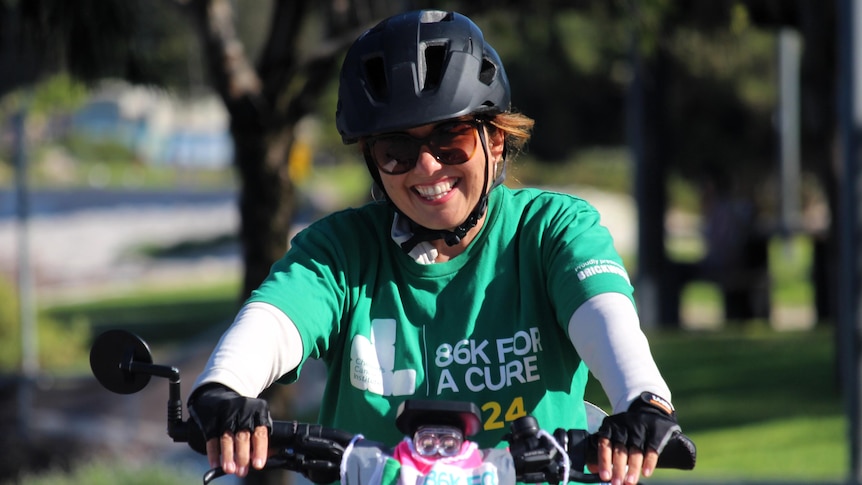 Female cyclist in a helmet, sunglasses, smiling.