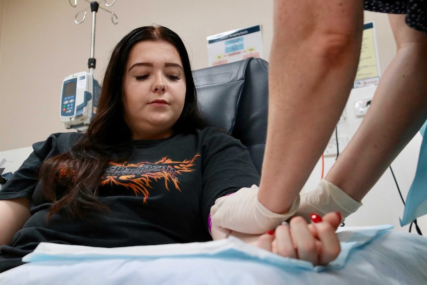 Young woman watches on while nurse takes blood from her arm