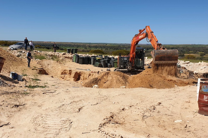 An excavator overseen by police digs a hole during a bikie-related search.