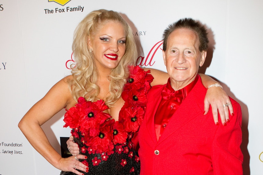 Geoffrey and Brynne Edelsten stand on the red carpet wearing bright red outfits