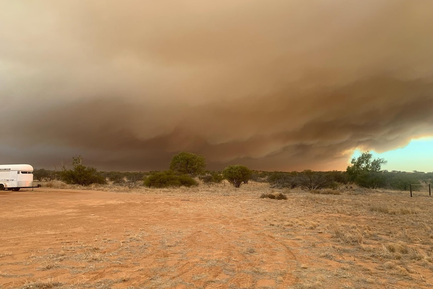 Land beneath a dark grey-orange bushfire smoke