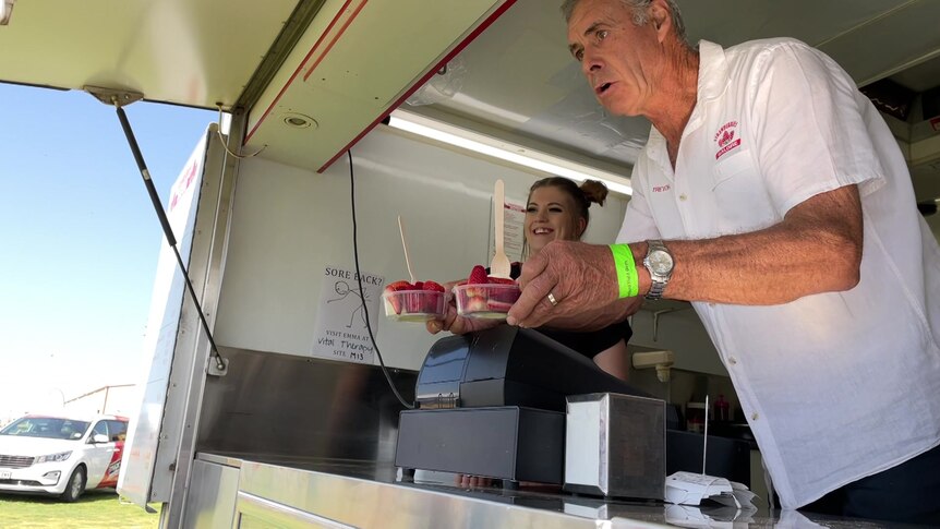 Trevor, a grey-haired, middle-aged man, serves up plastic cups of bright red strawberries from a food van.
