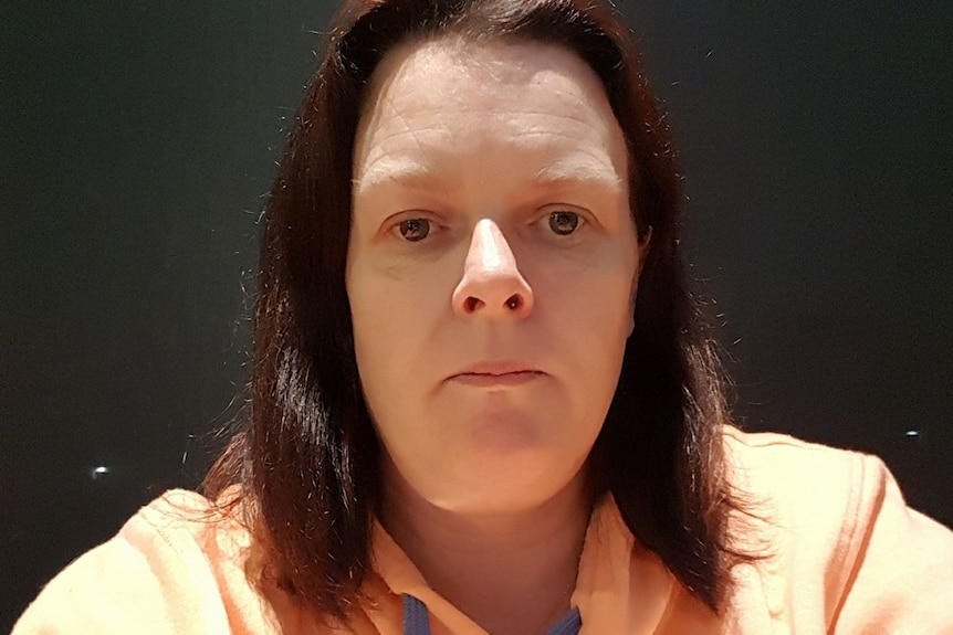 A selfie of a woman with dark hair, wearing an orange jumper