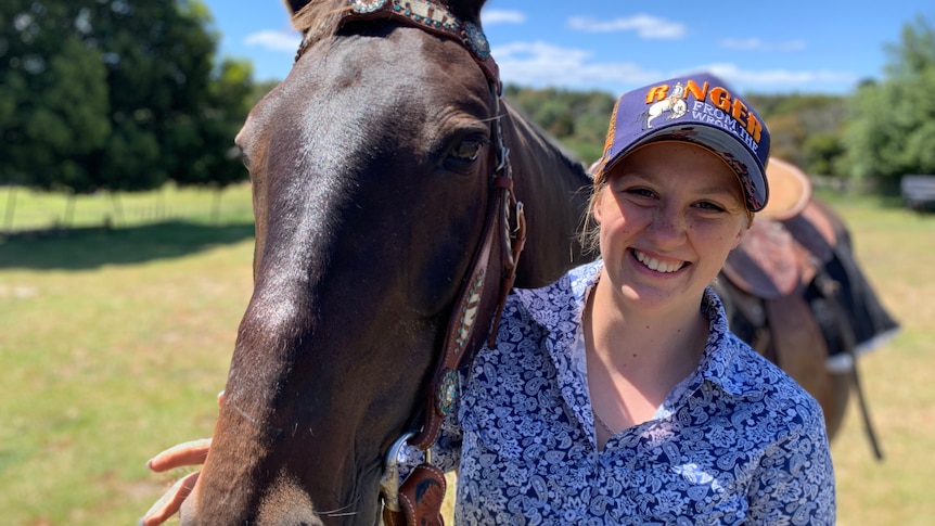 A young white woman in a floral blue shirt standing next to a horse 