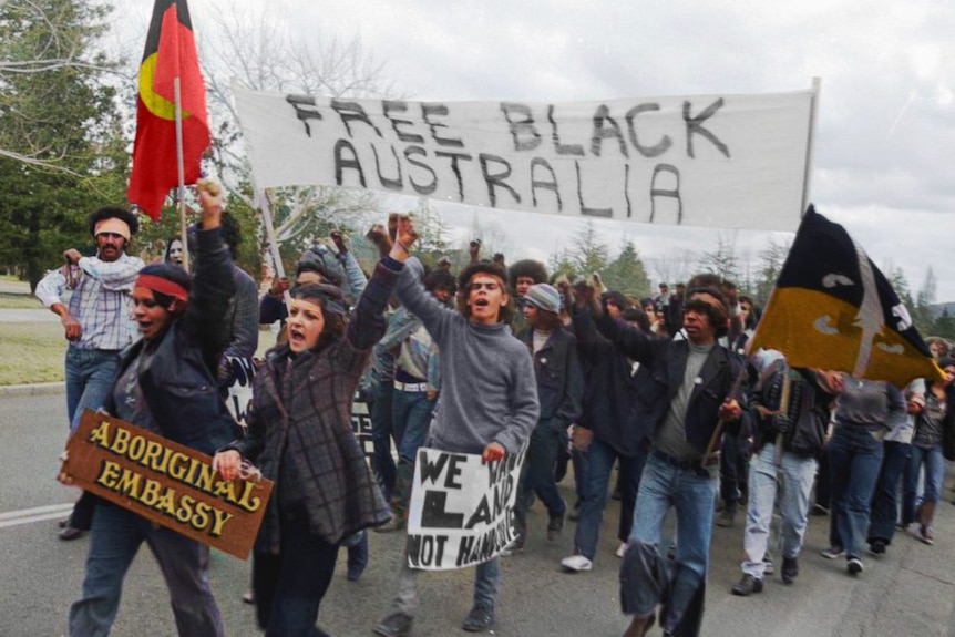 People marching and holding up the Aboriginal flag and a sign saying free black Australia